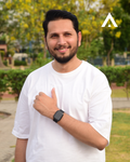 Man wearing a white t-shirt and black watch, standing outdoors with greenery in the background